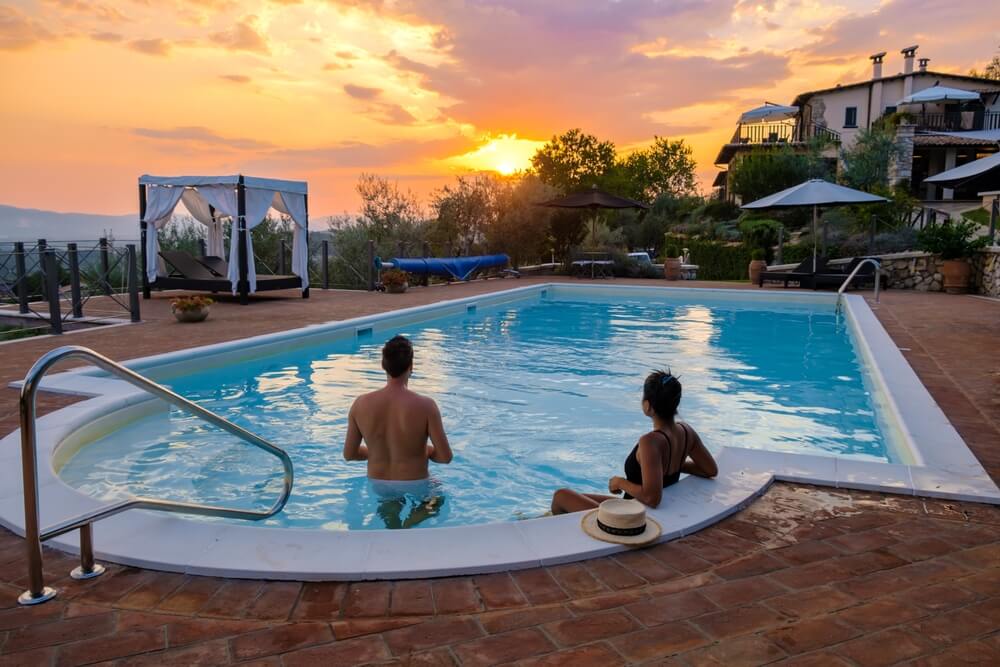 Par občuduje sončni zahod iz bazena ob luksuzni počitniški vili